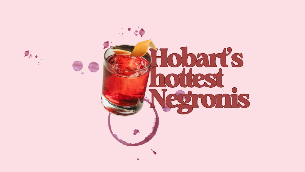 A glass of Negroni cocktail with an orange peel garnish sits against a light pink background. Bold red text reads “Hobart’s hottest Negronis” beside the glass, surrounded by artistic splashes and rings of red liquid.